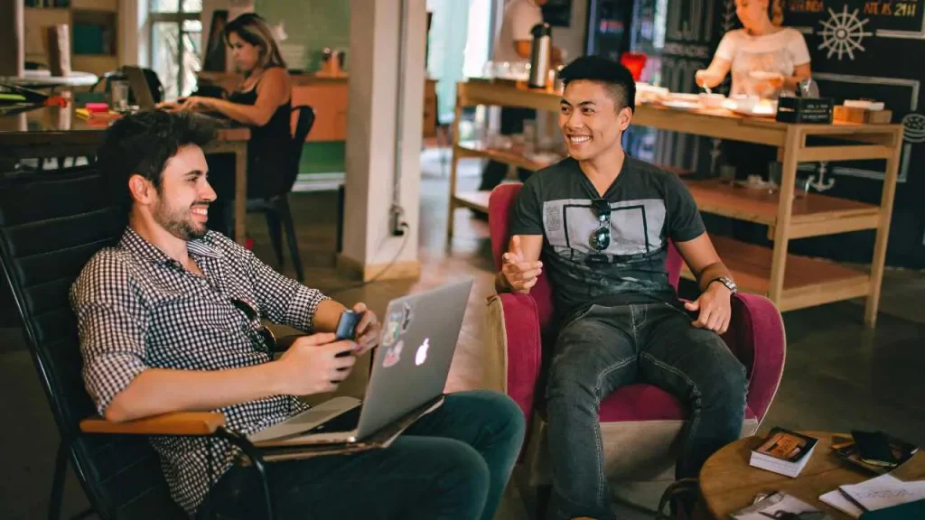 Two men discussing while sitting down. A laptop placed on the lap of one of the men.