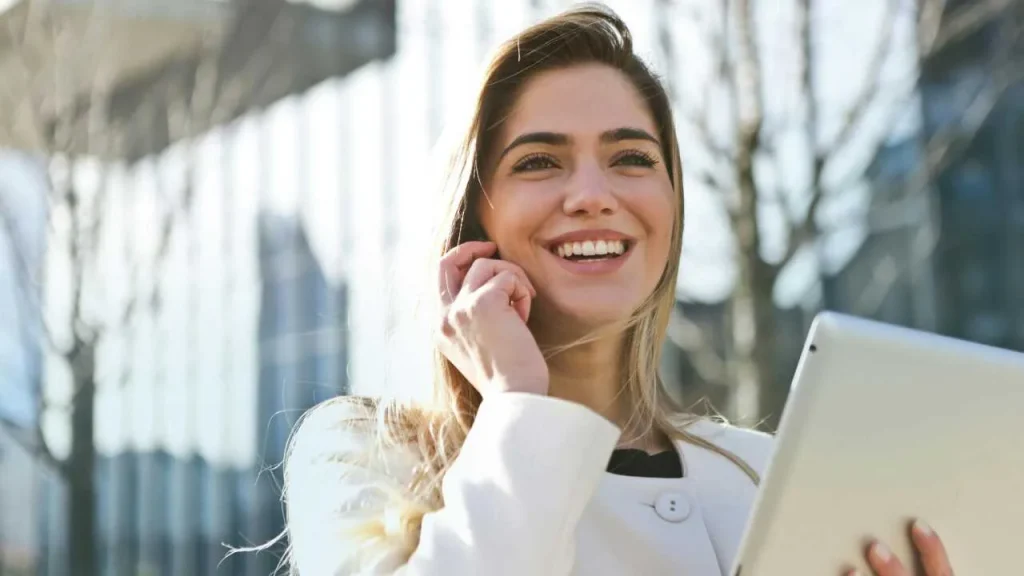 A lady in white suit, making a phone call and holding a laptop on her hands. 