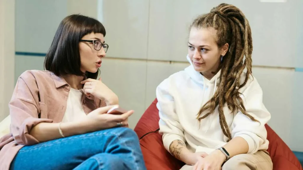 A lady actively discussing to another lady sitting on a chair. 
