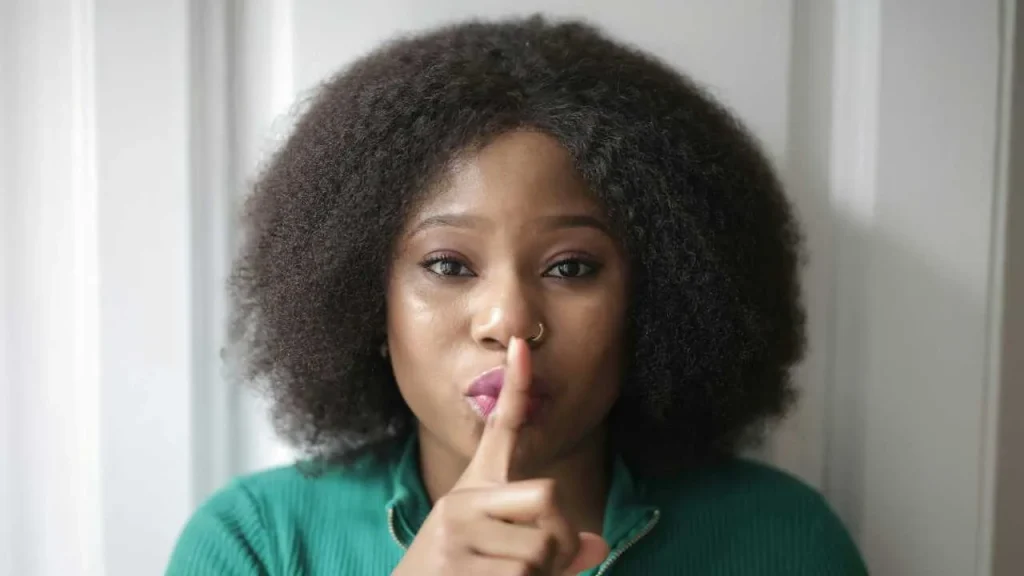A lady on green with her finger crossed on her lips. 