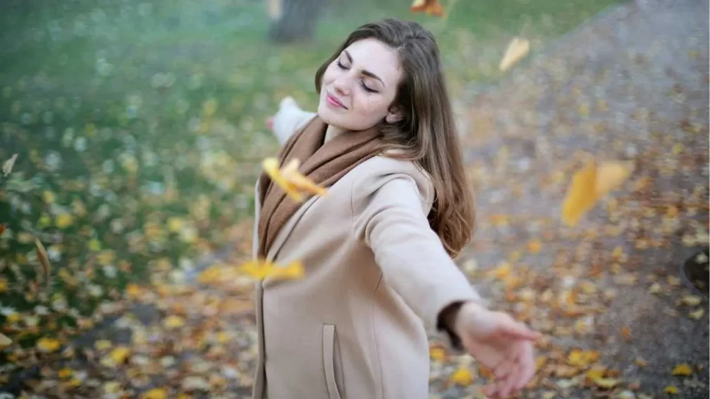 A lady in brown coat stretching her hands in nature