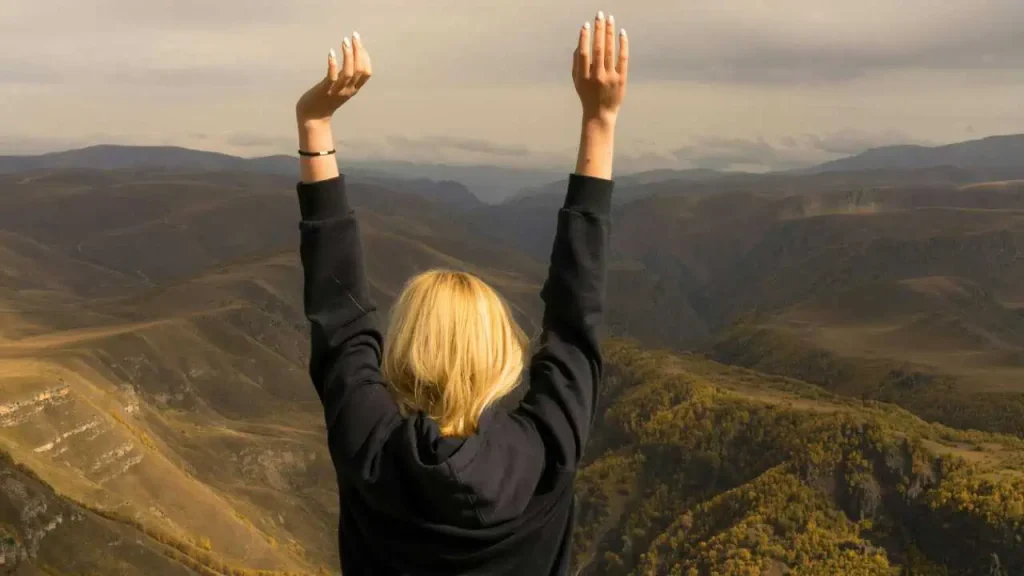 A woman raising her hands into the air on a mountain
