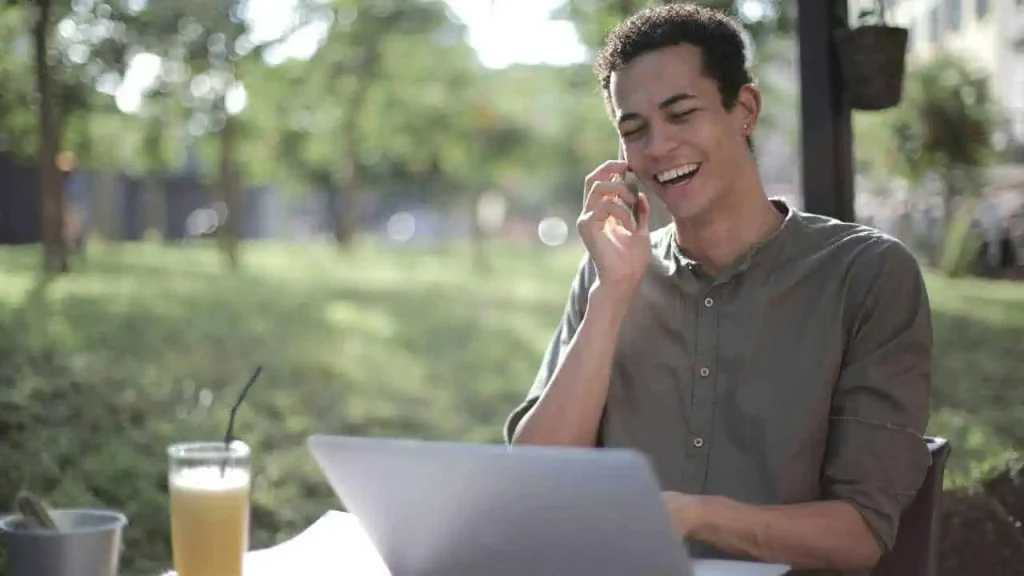A man happily making a phone call while typing his laptop