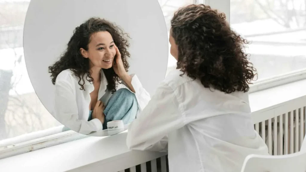 A lady in white sleeves looking at herself in the mirror as a step to practice self love