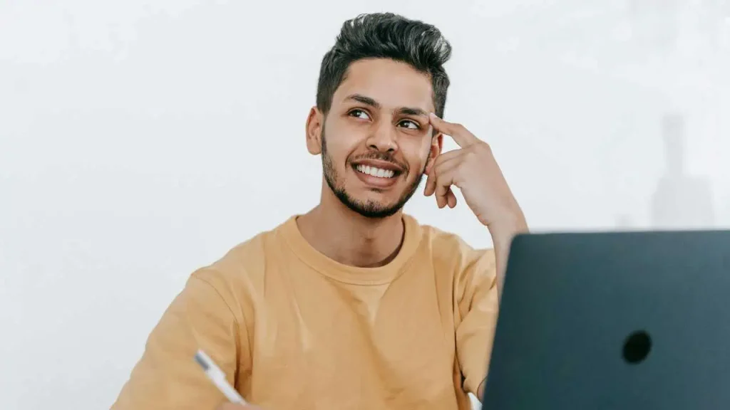 A man holding a white pen and sitting in front of a computer thinking—representing how to turn your passion into a career 