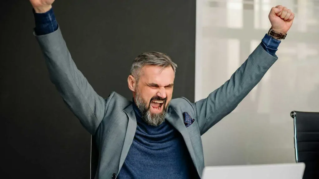 A man in ash-colored suit excited while throwing his hands into the air