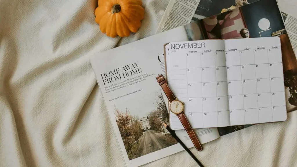 A wrist watch with a pen on a calendar and trip magazine