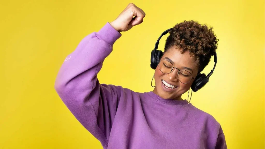 A lady on purple cardigan listening to music with her eyes closed and one hand raised up