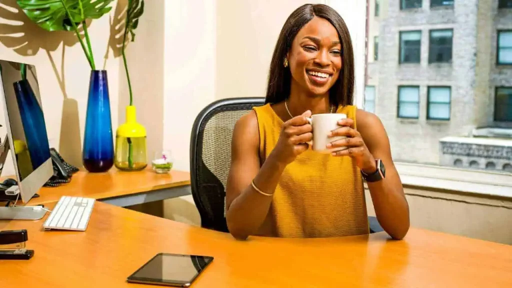 A lady smiling and holding a cup of coffee while sitting in front of a desk