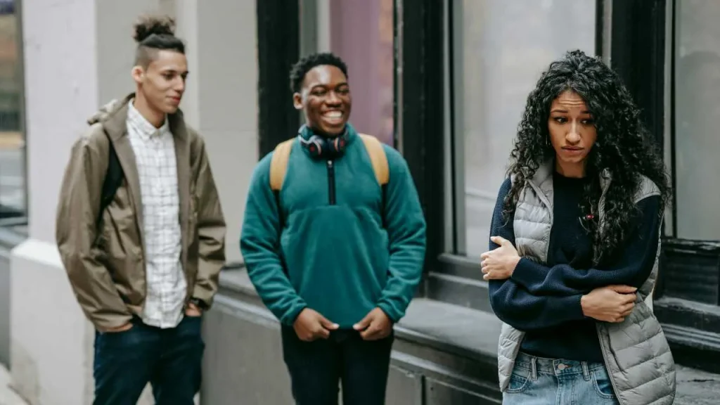 Two boys laughing at a girl who looks sad