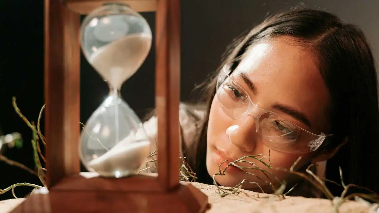 A lady on glasses looking at an hour glass depicting patience is a virtue