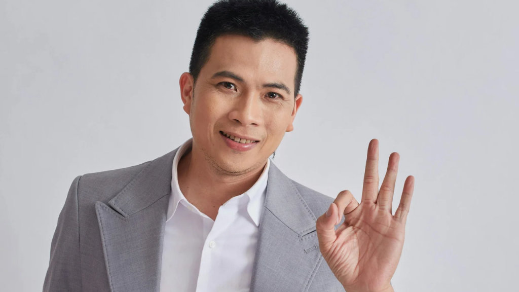 A man in a grey suit showing an O.K finger symbol