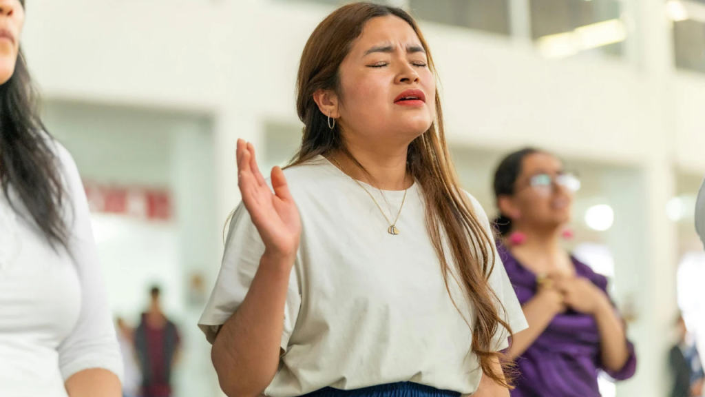 A lady on a white top praying depicting how to stop being a people pleaser and start living God's approval